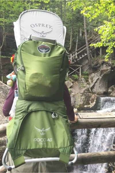 baby in a green Osprey poco ag plus backpack hiking carrier by a waterfall