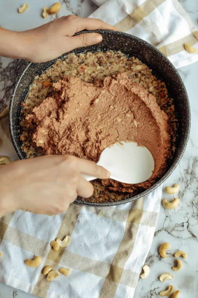 spreading the raw chocolate date filling on top of the nut crust in a cake pan