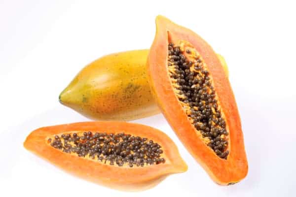 whole ripe papaya with yellow skin and green spots next to sliced open papaya