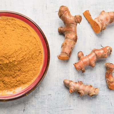 closeup of fresh turmeric root and powder in a bowl on gray background