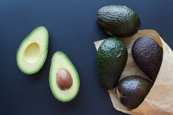 whole and halved haas avocados wrapped in paper on dark countertop