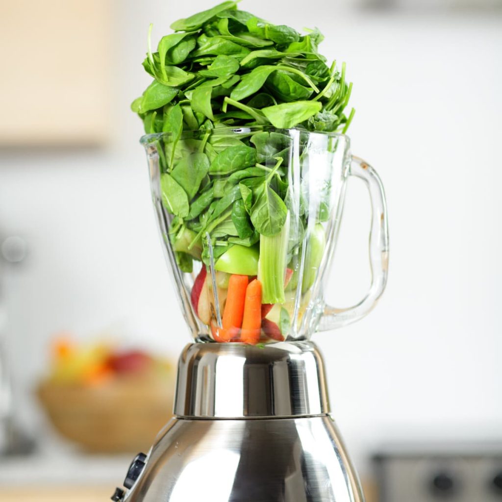 Overflowing blender full of spinach, carrots, celery, and apples to hide vegetables in food for picky eaters