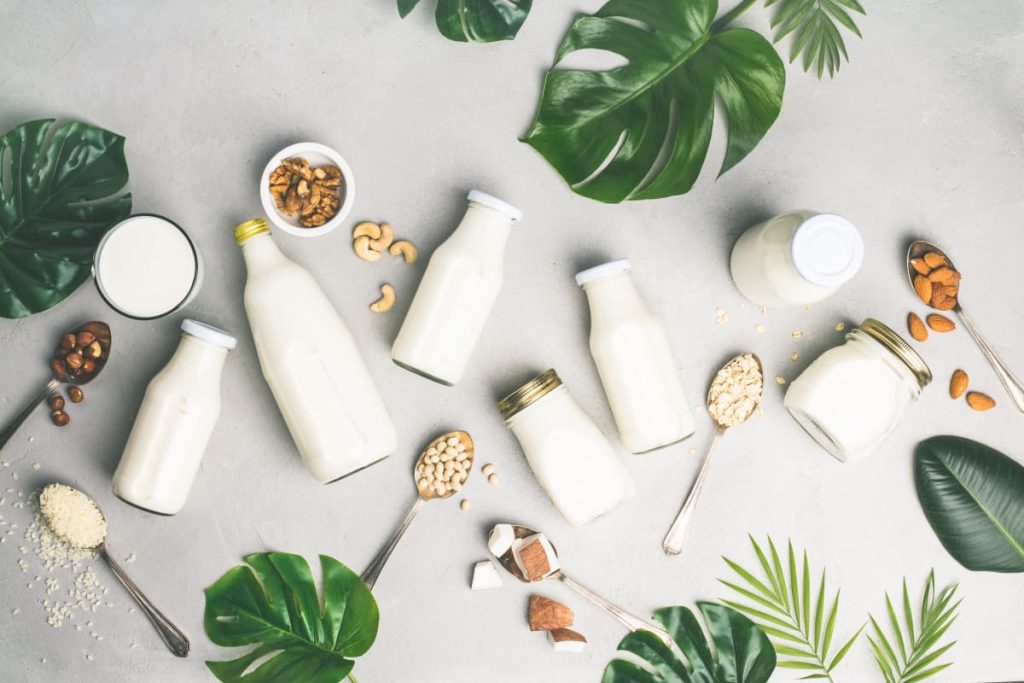 dairy free milk and yogurt in glass bottles with ingredients on spoon flat lay